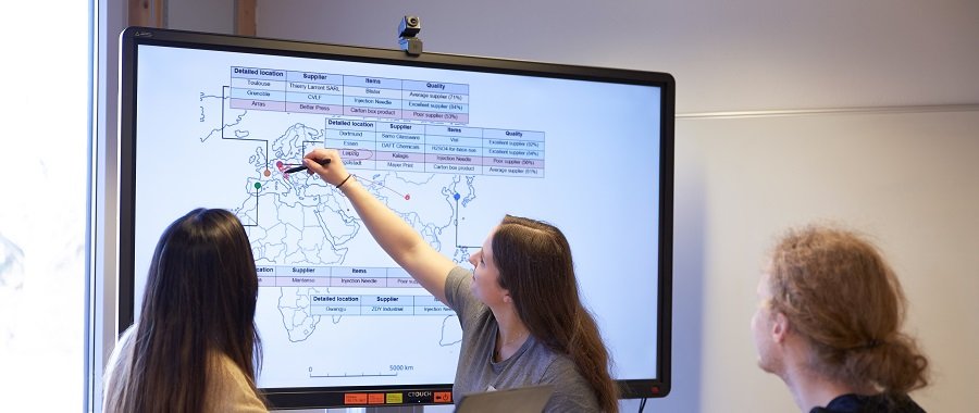 Drei Studierende analysieren europäische Wirtschaftsdaten an einem großen Monitor.