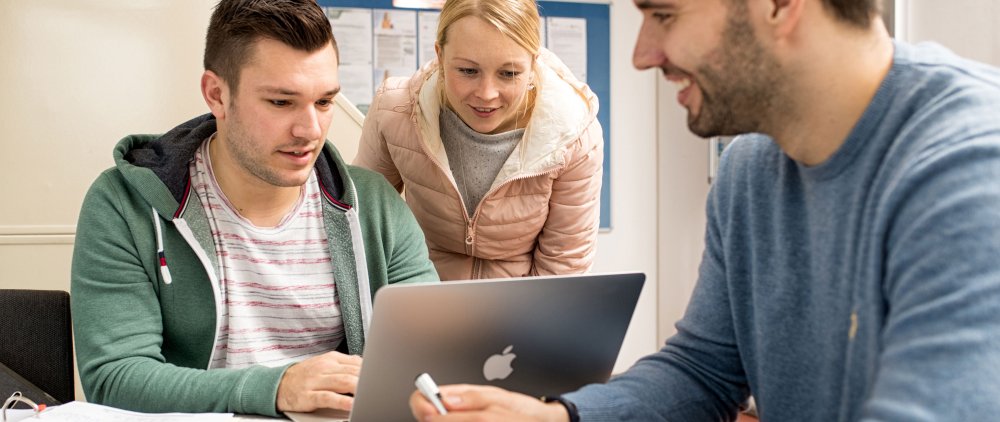 Three students looking at a notebook standing between then.